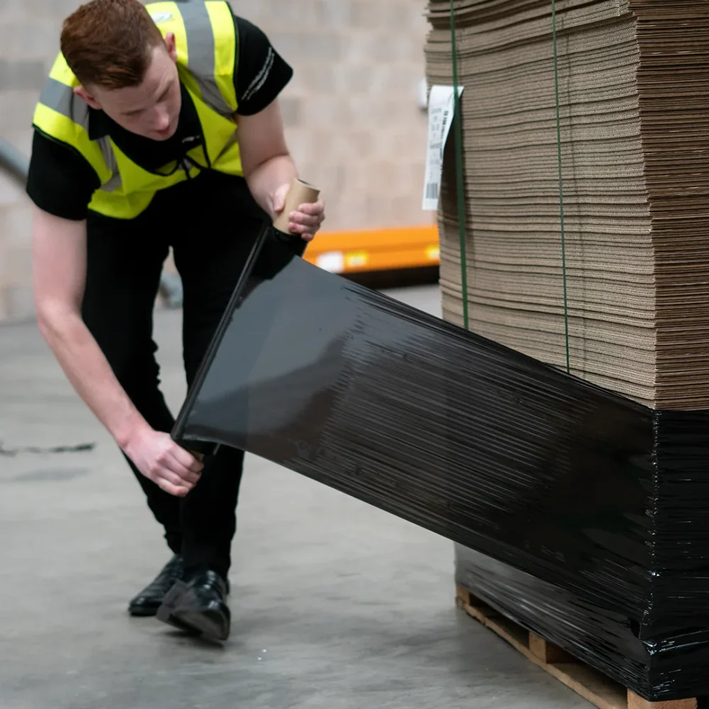 Warehouse worker pulls black pallet wrap around the base of a pallet.