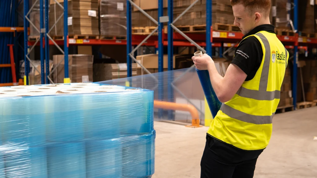 Worker wraps pallet in blue pallet film wrap.