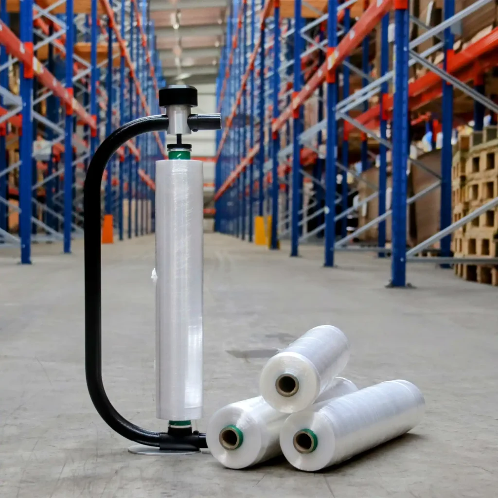 Stretch film roll attached to a hand film dispenser, with three film rolls laid next to it in a warehouse floor