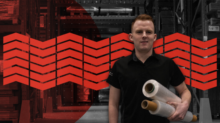 A warehouse professional holding two large rolls of clear stretch film in a storage facility with industrial racking in the background.