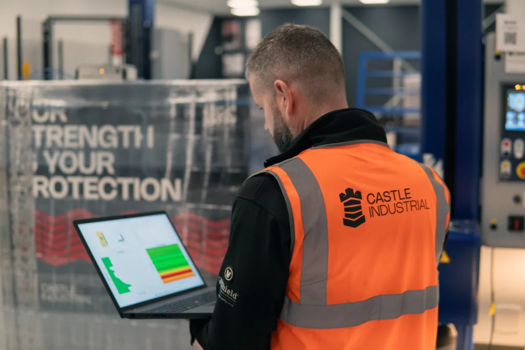 Technical Consultant looking at load containment readings on a laptop, with wrapped pallet in the background