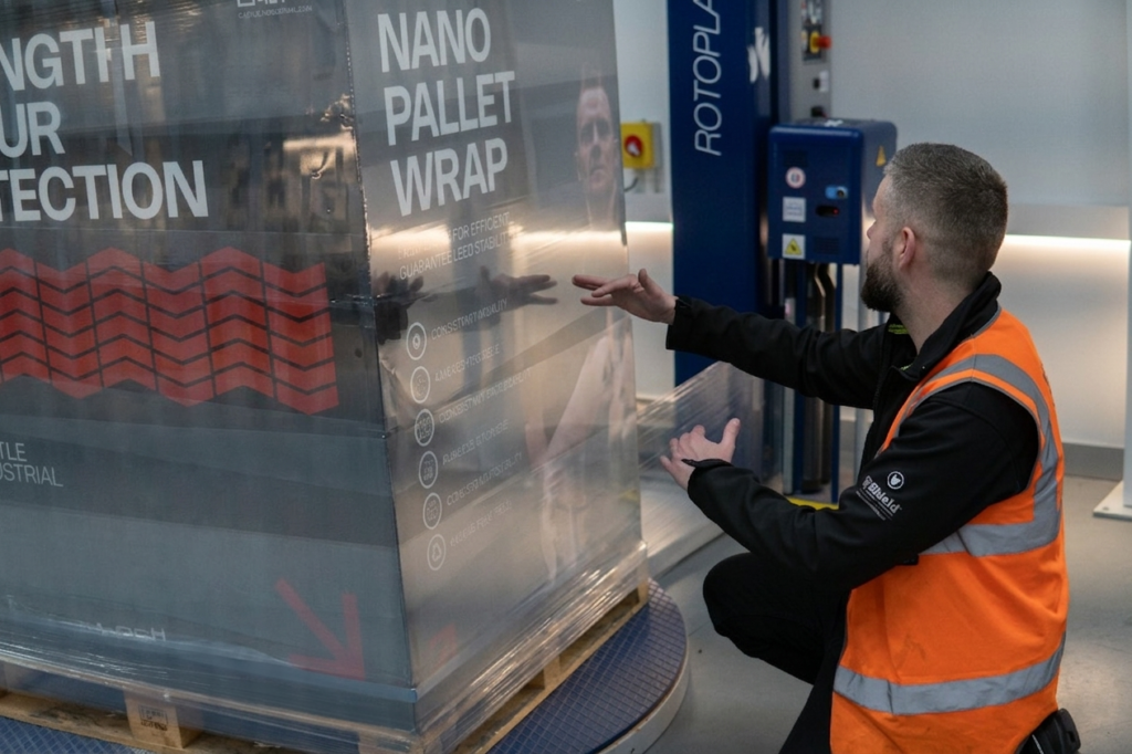 Load Stability technician in high vis kneeling by a wrapped pallet