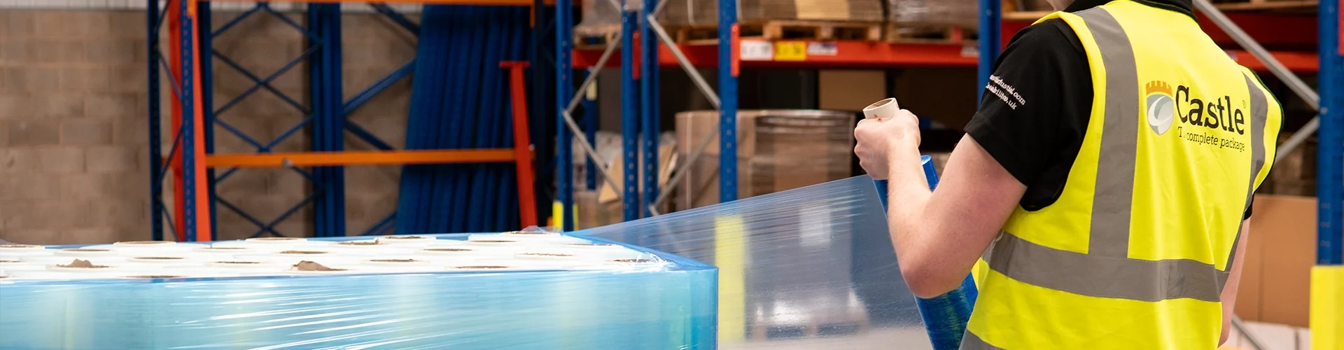 Employee pulls blue pallet wrap around a bulky pallet of film.