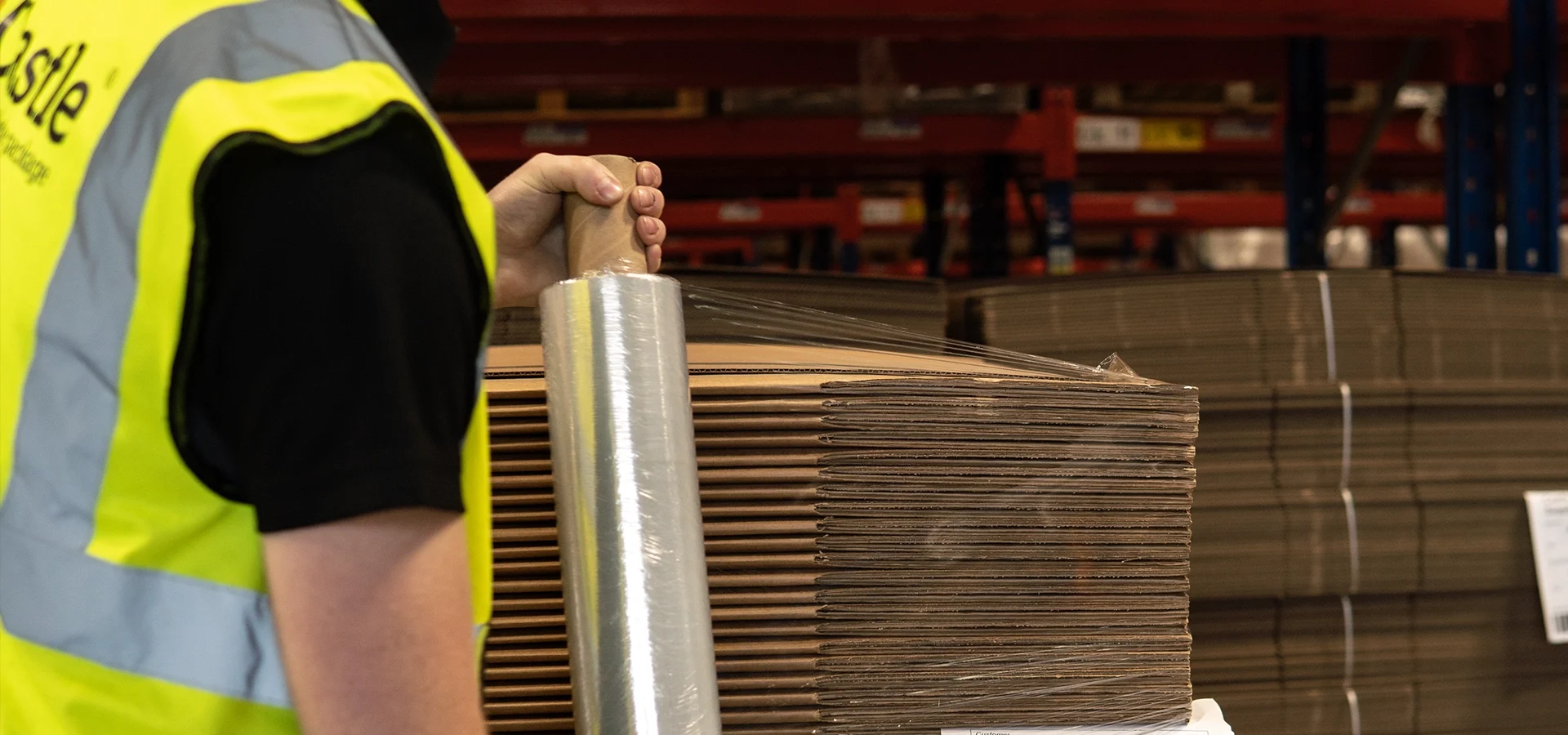 Warehouse worker wraps pallet in clear film wrap.